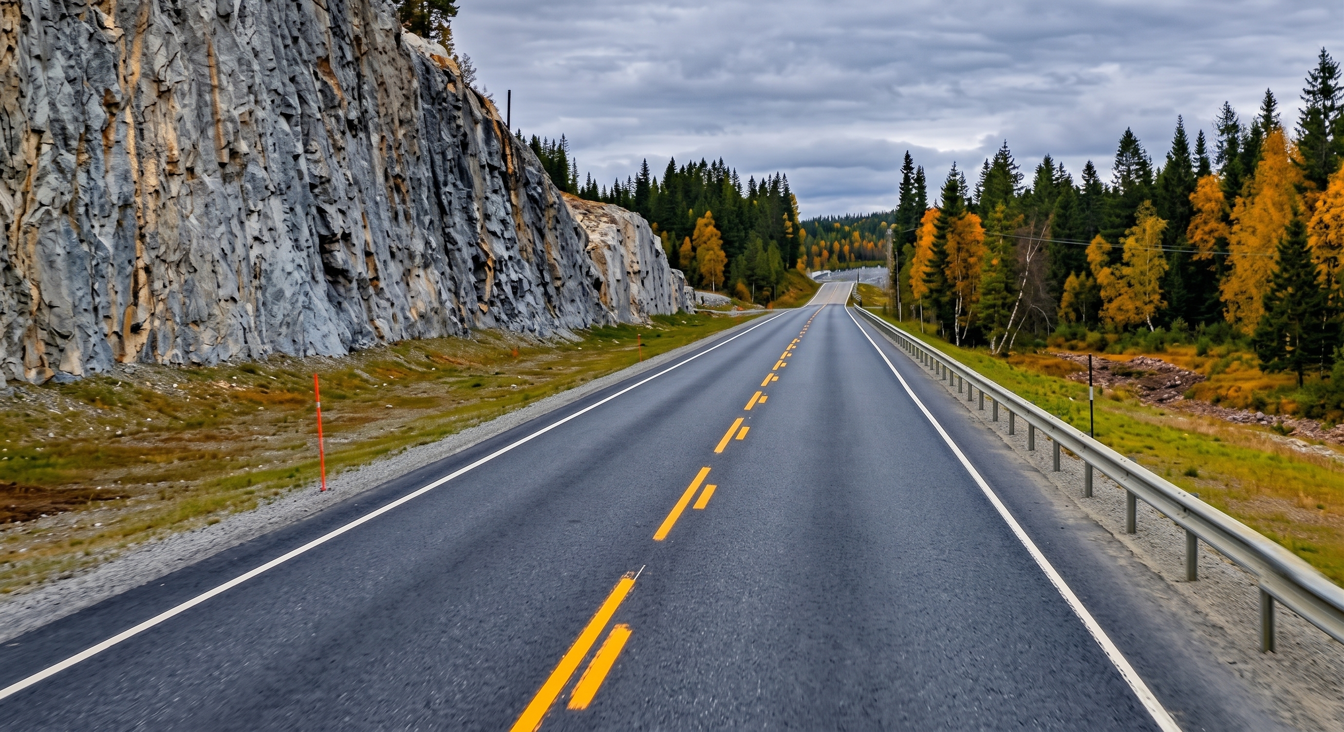 A rural Norwegian road beside a rock face and autumn forest